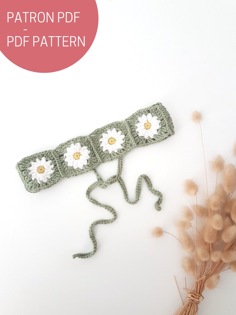 May include: A green crocheted headband with white daisy flowers. The headband has two long ties that can be tied at the back of the head.