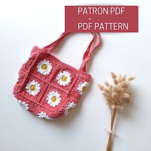 Puede incluir: Una bolsa de crochet con un patrón de margarita en rosa y blanco. La bolsa tiene una correa larga y está hecha con un punto de granny square. El texto "PATRON PDF - PDF PATTERN" está sobre un fondo rojo.