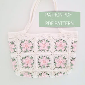 K&ouml;nnte beinhalten: Eine wei&szlig;e H&auml;kel-Tragetasche mit rosa und gr&uuml;nen Blumendetails. Die Tasche hat zwei Henkel und ist mit einem quadratischen Stichmuster gearbeitet. Der Text "PATRON PDF - PDF PATTERN" ist auf dem Bild zu sehen.