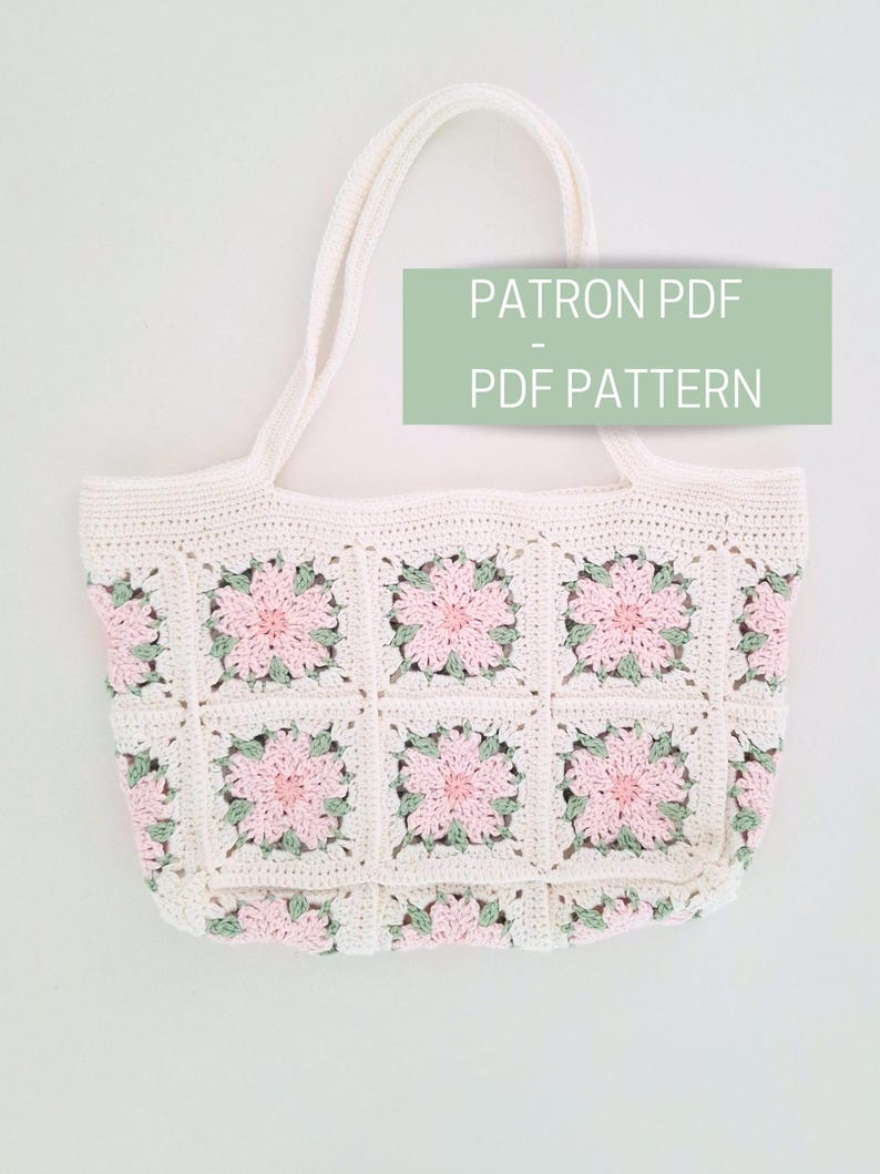 K&ouml;nnte beinhalten: Eine wei&szlig;e H&auml;kel-Tragetasche mit rosa und gr&uuml;nen Blumendetails. Die Tasche hat zwei Henkel und ist mit einem quadratischen Stichmuster gearbeitet. Der Text "PATRON PDF - PDF PATTERN" ist auf dem Bild zu sehen.