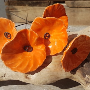 Puede incluir: Cinco formas de flores de cerámica naranja con un tallo de alambre. Las flores tienen una superficie texturizada y un pequeño anillo de metal en el centro.