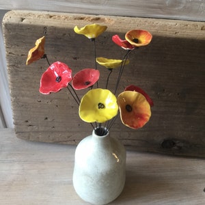 Könnte beinhalten: Ein Strauß Keramikblumen in einer weißen Vase. Die Blumen sind gelb und rot mit einer strukturierten Oberfläche. Die Vase hat eine einfache, abgerundete Form.
