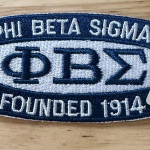 May include: Embroidered patch in navy blue and white, featuring the Greek letters ΦΒΣ and the text "PHI BETA SIGMA" and "FOUNDED 1914". Includes a small, rectangular sticker with the fraternity's logo.