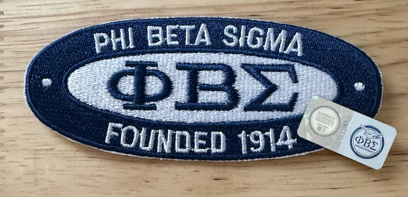 May include: Embroidered patch in navy blue and white, featuring the Greek letters &Phi;&Beta;&Sigma; and the text "PHI BETA SIGMA" and "FOUNDED 1914". Includes a small, rectangular sticker with the fraternity's logo.