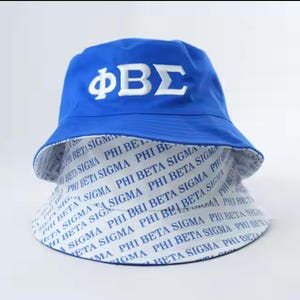 May include: A blue and white reversible bucket hat with the letters "ΦΒΣ" embroidered on the front. The hat is made of a lightweight fabric and has a wide brim. The inside of the hat is white with the letters "PHI BETA SIGMA" repeated in blue.