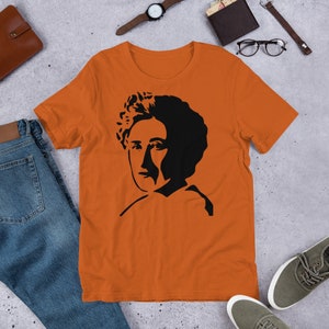 May include: Orange short-sleeved t-shirt with a black silhouette of a woman with curly hair.