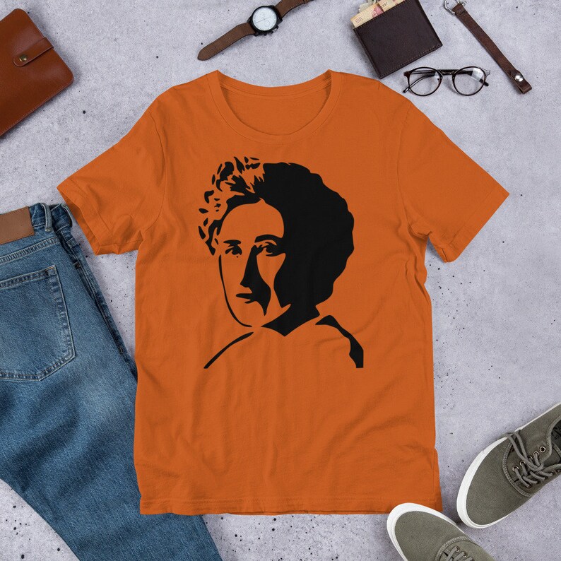 May include: Orange short-sleeved t-shirt with a black silhouette of a woman with curly hair.
