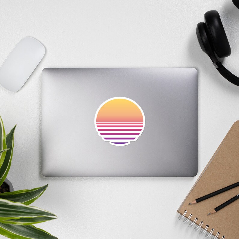 May include: A round sticker with a retro sunset design. The sun is yellow, orange, and pink with purple and white stripes.