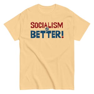 May include: A pale yellow t-shirt featuring the text "SOCIALISM IS BETTER!" in red and blue block letters. The shirt is a short-sleeved, casual style.