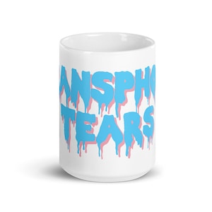 May include: White ceramic mug with the text "Transphobe Tears" in blue and pink dripping letters.
