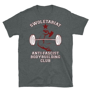 May include: A dark grey t-shirt with a red graphic of a bicep lifting a barbell with a red star and the text "SWOLETERIAT ANTI-FASCIST BODYBUILDING CLUB".