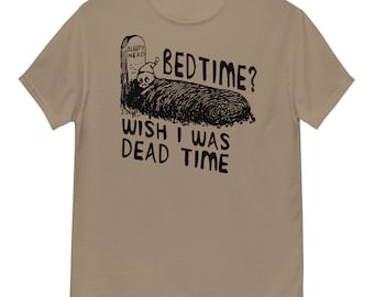 Peut inclure: Un t-shirt beige avec un graphique noir d'une personne dormant dans un cercueil avec le texte "Bedtime? Wish I was Dead Time" imprimé dessus.