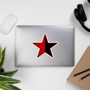 May include: A red and black star sticker with a white outline. The star is divided diagonally, with the top half red and the bottom half black.
