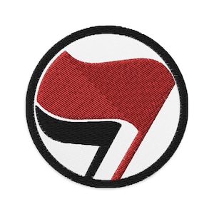 May include: A red and black embroidered patch with a stylized flag in a circle. The flag is red with a black outline and is in the shape of a stylized fist.