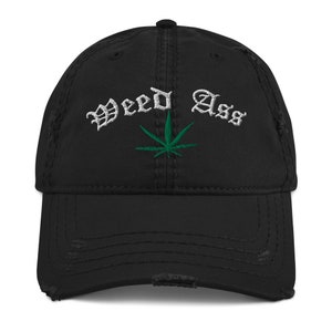 以下が含まれることがあります： 白い刺繍で「Weed Ass」と緑色のマリファナの葉が刺繍された、黒色のダメージ加工が施されたベースボールキャップです。