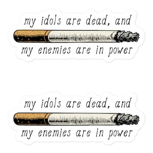 May include: Two white stickers with black text and a brown and white cigarette illustration. The text reads "my idols are dead, and my enemies are in power".