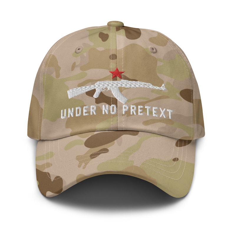May include: A camouflage baseball cap with a white embroidered AK-47 and the text "UNDER NO PRETEXT" in white. The star on the AK-47 is red.