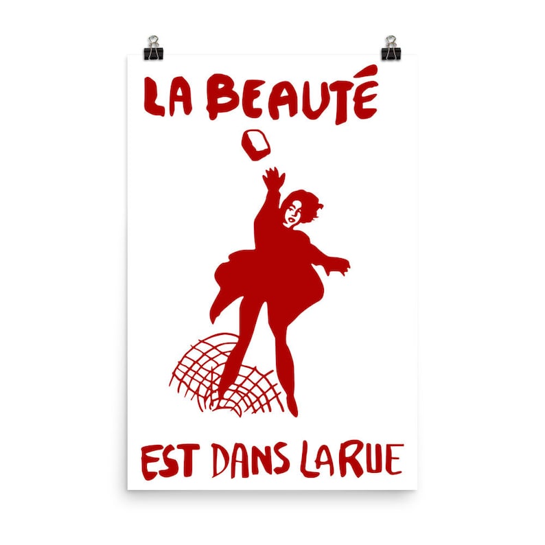 May include: A red silhouette of a person throwing a brick at a fence with the text "LA BEAUT&Eacute; EST DANS LA RUE" in red.