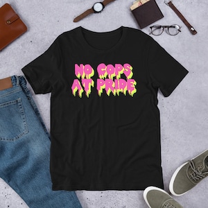 May include: Black t-shirt with a pink and yellow graphic that says "NO COPS AT PRIDE".