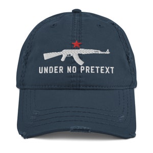 May include: A distressed blue baseball cap with a white embroidered image of an AK-47 rifle and the text "UNDER NO PRETEXT".