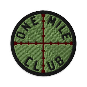 Könnte beinhalten: Ein grüner gestickter Aufnäher mit schwarzem Rand und roten Fadenkreuzen. Der Text "ONE MILE CLUB" ist in einem Kreis um die Fadenkreuze geschrieben.