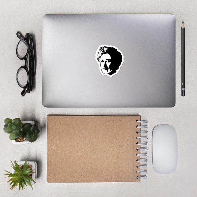May include: A black and white sticker of a person's face with curly hair. The sticker is on a silver laptop computer.