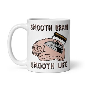 May include: White ceramic mug with a black outline of a brain being ironed by a silver iron with a brown handle. The text "SMOOTH BRAIN SMOOTH LIFE" is printed in black on the mug.