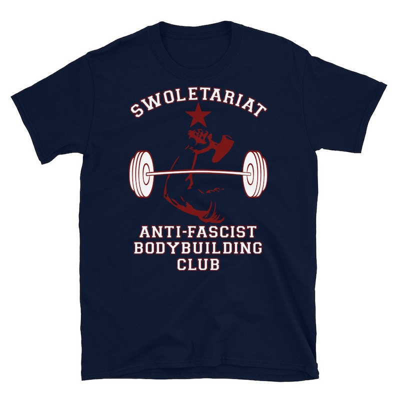 May include: A navy blue t-shirt with the text "Swole-tariat Anti-Fascist Bodybuilding Club" in white and red lettering. A red star and a red silhouette of a bicep lifting a barbell are also featured on the shirt.