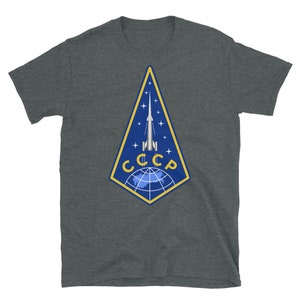 May include: A dark heather grey t-shirt with a graphic of a rocket launching from a globe with the text "CCCP" in yellow letters.