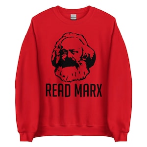 May include: A bright red crewneck sweatshirt featuring a black graphic print of Karl Marx's face centered on the chest. Below the portrait, the text READ MARX is printed in a bold, black, sans-serif font. The garment has long sleeves.