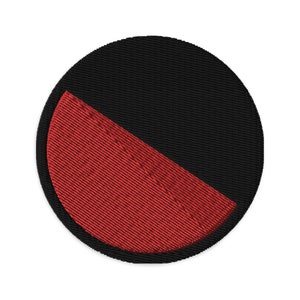 May include: A round black and red patch with a diagonal line dividing the colors. The red section is textured.