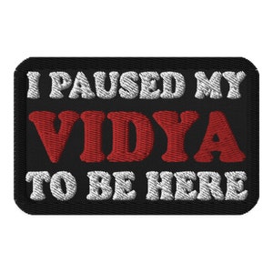 May include: Black embroidered patch with white text that reads "I paused my vidya to be here" with the word "vidya" in red.