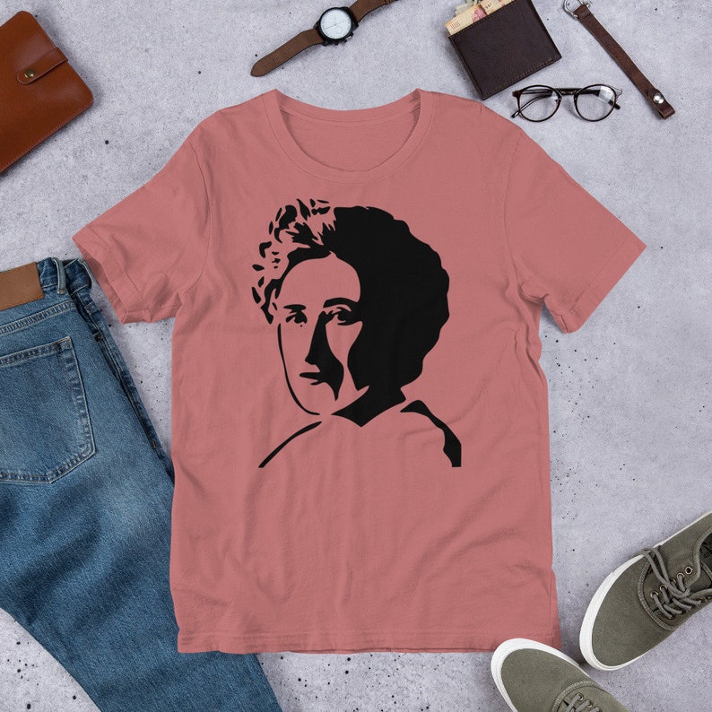 May include: A pink t-shirt with a black silhouette of a woman's face.