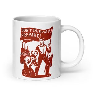 Op de afbeelding: Witte keramische mok met een rode illustratie. Het ontwerp bevat de tekst "DON'T DESPAIR, PREPARE!" op een banner, met figuren en industriële gebouwen. De mok heeft een gebogen handvat.