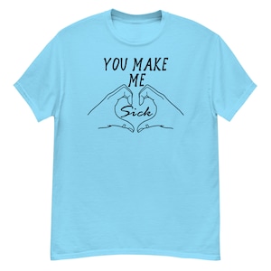 May include: Light blue t-shirt with black text that reads "You make me sick" with a heart shape formed by two hands.