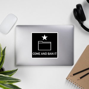 May include: A black and white sticker with a white folder icon and a star on a black background. The text "COME AND BAN IT" is below the icon.
