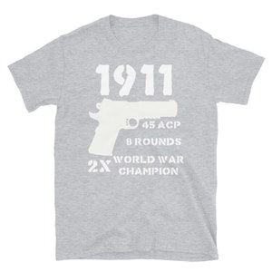 May include: Gray t-shirt with a white graphic of a 1911 pistol, the text "45 ACP", "8 Rounds", "2X World War Champion", and a silhouette of a pistol.