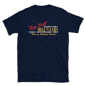 May include: A navy blue t-shirt with a red and yellow graphic that reads "Big Bill" Baltimore's Filthiest "Hell's Cars" Bad Deals - Cars That Break Down - Thieves "Home of Challenge Pissing"