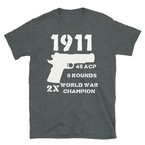 May include: A dark gray t-shirt with a white graphic design of a 1911 pistol, the text "45 ACP", "8 Rounds", "2X World War Champion", and the number "1911".