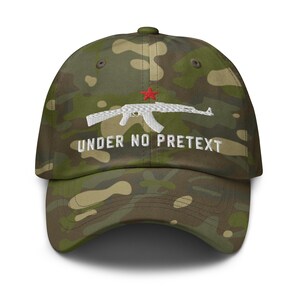 May include: A camouflage baseball cap with a white embroidered AK-47 rifle and the text "UNDER NO PRETEXT" in white. The rifle has a red star on the receiver.