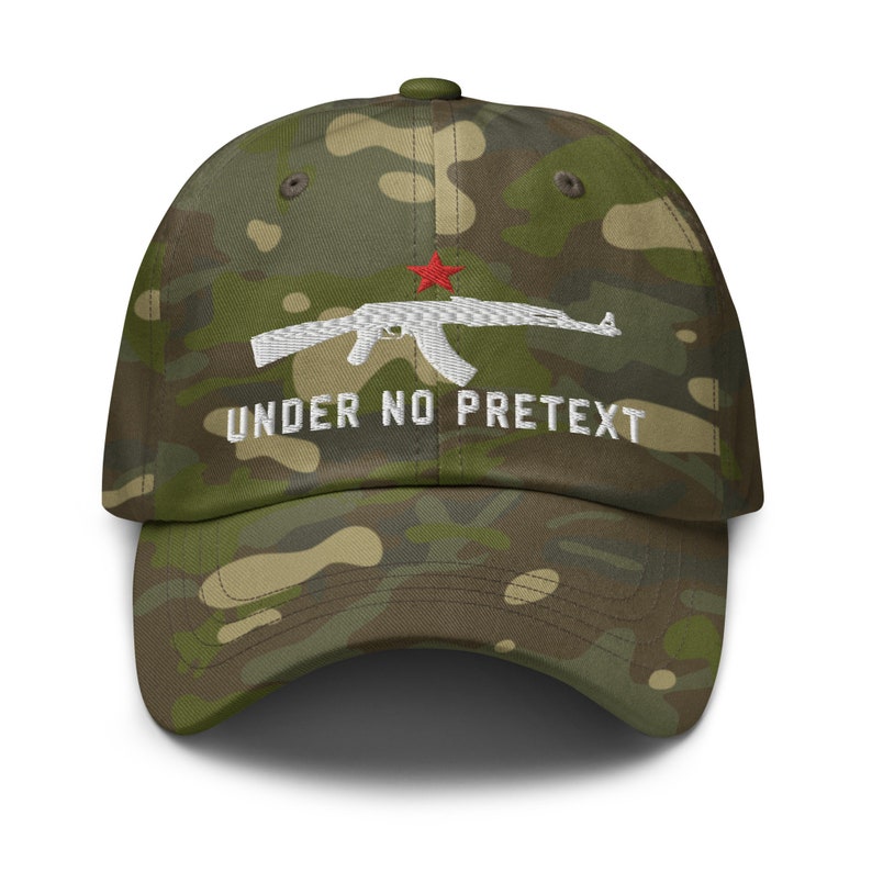 May include: A camouflage baseball cap with a white embroidered AK-47 rifle and the text "UNDER NO PRETEXT" in white. The rifle has a red star on the receiver.
