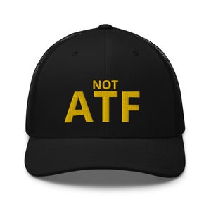 Puede incluir: Gorra de camionero negra con un dise&ntilde;o bordado en amarillo que dice "NOT ATF".