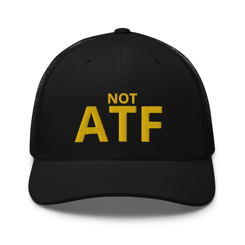 Puede incluir: Gorra de camionero negra con un dise&ntilde;o bordado en amarillo que dice "NOT ATF".