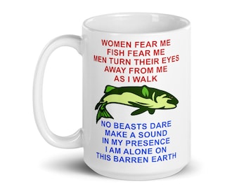 Könnte beinhalten: Eine weiße Keramiktasse mit einer Illustration eines grünen und gelben Fisches und rotem Text, der lautet: "Frauen fürchten mich, Fische fürchten mich, Männer wenden ihre Augen von mir ab, wenn ich gehe. Keine Bestie wagt es, ein Geräusch in meiner Gegenwart zu machen, ich bin allein auf dieser kargen Erde."