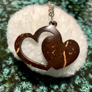 May include: A brown coconut shell keychain with two intertwined heart shapes. The keychain is attached to a silver chain.