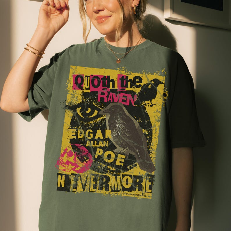 May include: An olive green t-shirt with a graphic design inspired by Edgar Allan Poe's poem, "The Raven." The design includes the text "Quoth the Raven," "Edgar Allan Poe," and "Nevermore," alongside illustrations of a raven and a skull.