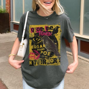 May include: Dark grey t-shirt with a graphic design inspired by Edgar Allan Poe's poem "The Raven." The design includes a raven illustration, the words "Quoth the Raven," "Edgar Allan Poe," and "Nevermore" in a distressed style.