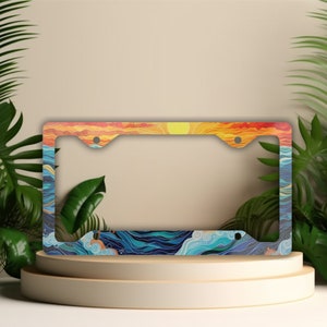 May include: License plate frame featuring a sunset over the ocean design. The frame has a colorful illustration of a sunset with orange, yellow, and red hues, and ocean waves in shades of blue and white. The frame is rectangular with rounded corners.