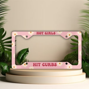 May include: Pink license plate frame with a white daisy pattern and the text "HOT GIRLS HIT CURBS" in red.