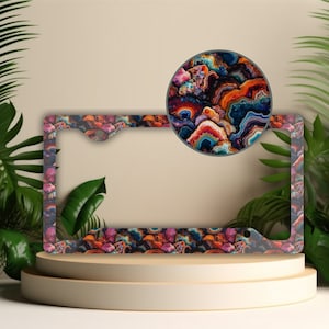 May include: A colorful license plate frame with a swirling, abstract pattern in shades of pink, orange, blue, and green. The frame is made of metal and has a glossy finish.